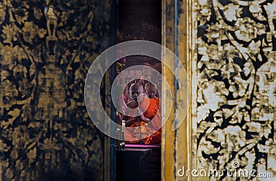 Looking through the the ajar door buddhist monks sitting praying and pay respect Buddha image in main vihan Editorial Stock Photo