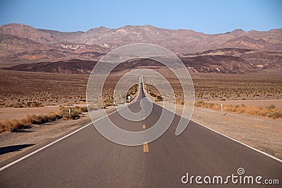 Looking down the middle of a long straight desert road with no one in site for miles in the Death Valley Stock Photo