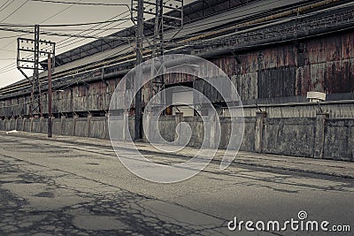 Looking down a wore out empty street next to an abandoned industrial factory with crumbling exterior Stock Photo