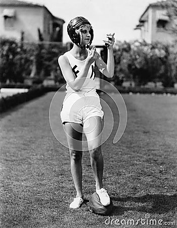 Looking good for the team, a young woman in a football helmet looking into a mirror and putting on make up Stock Photo