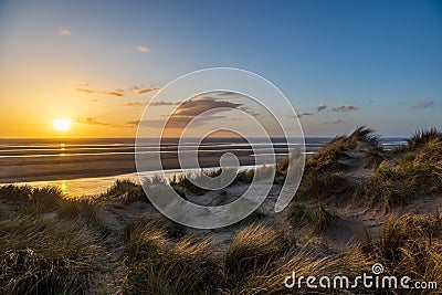 Sunset at the beach, with marram grass covered sand dunes in the foreground Stock Photo