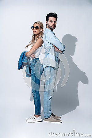 Looking trendy. Full length of beautiful young couple smiling while standing back to back against grey background Stock Photo