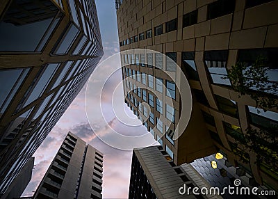 Looking up at beautiful dusk pink blue summer sunset sky surrounded by tall high rise tower block sky scrapers. Stock Photo