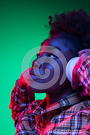 Close-up happy young girl, student listening to music in headphones isolated on dark green studio background in purple Stock Photo