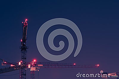 Looking up at group of tall and high tower cranes with red position lights at large construction site for housebuilding at night Stock Photo