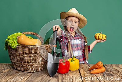 Emotional little girl, cheerful kid in image of farmer, gardener having fun with seasonal vegetables isolated on green Stock Photo