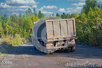 Lorry dump truck rides on a dirt road against the background of the forest and blue summer sky Stock Photo