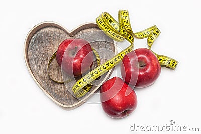 Lose Weigh. Close Up of Measuring Yellow Tape Ties Around Red Apples in Wooden Heart shape box. Isolated on white background. hori Stock Photo