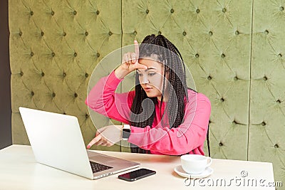 Loser! Portrait of unhappy rude young girl freelancer with black dreadlocks hairstyle in pink blouse are sitting in cafe and Stock Photo