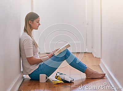 Losing herself in a sea of words. a young woman reading a book while sitting on the floor at home. Stock Photo