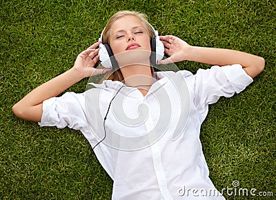 Losing herself to the music. High angle shot of a woman lying on a grassy field listening to music with her eyes closed. Stock Photo