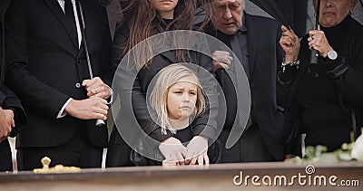 Loss, grief and people at funeral with umbrella, flowers and coffin, family with sad child at service in graveyard Stock Photo