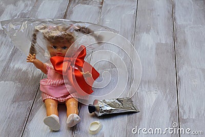 Lost childhood. Drugs and children. Doll with plastic bag, red satin bow, glue tube on light wooden background Stock Photo