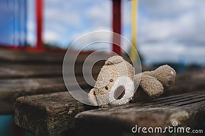 Lost teddy bear lying on wooden bridge at playground in gloomy day, Lonely and sad face brown bear doll lied down alone in the Stock Photo