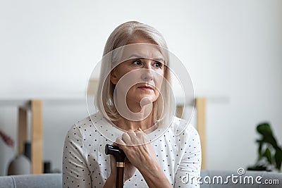 Lost in thoughts middle aged female retiree holding wooden cane. Stock Photo