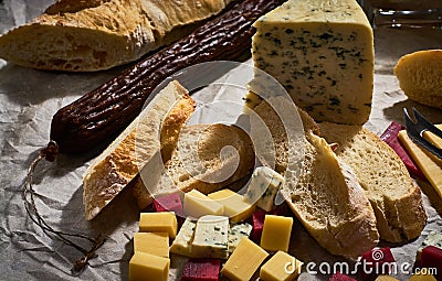 A lot of different types of cheese with dry sausage and fresh bagette, wine glasses on kraft paper. Stock Photo