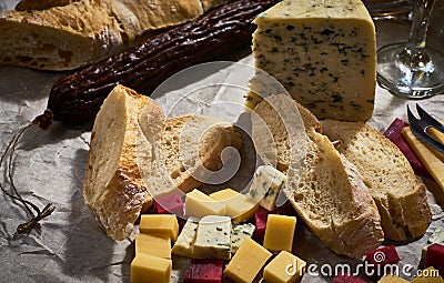 A lot of different types of cheese with dry sausage and fresh bagette, wine glasses on kraft paper. Stock Photo