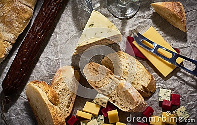 A lot of different types of cheese with dry sausage and fresh bagette, wine glasses on kraft paper. Stock Photo