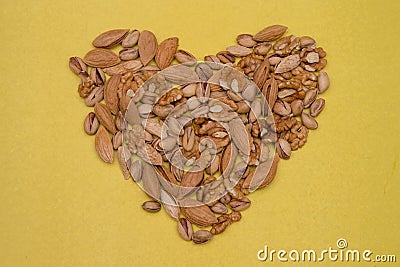 A lot of dried nuts are laid out on a yellow background of textured paper in the shape of a heart. Peeled walnuts, pistachios and Stock Photo
