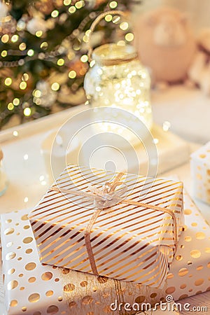 A lot of packing handmade gift boxes lying on the table near Christmas tree in the midst of golden lights, glowing garland, candle Stock Photo