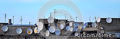 A lot of satellite television antennas on the rooftop under a bl Stock Photo