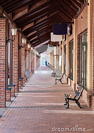 Lots of boutiques. Long corridor. The perspective of the street. Pillars with lanterns near the bench. Red brick building Stock Photo