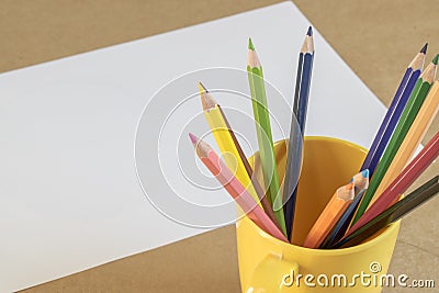 A lots of colour pencil in yellow cup and white paper on background , prepare drawing Stock Photo