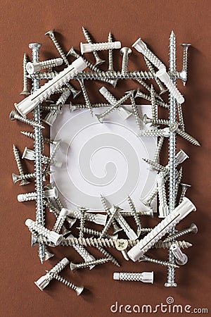 Lots of gray plastic dowels and galvanized metal screws on a brown background Stock Photo