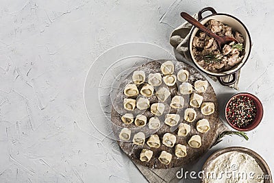 Lots of ready-to-cook pork dumplings on a large wooden board with flour and meat in bowls Stock Photo