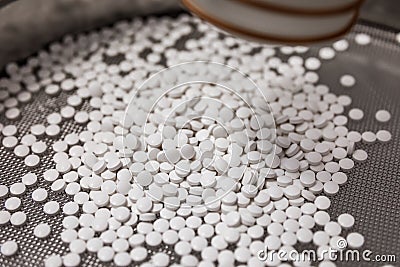 Lots of white tablets are poured onto a special sieve. Abstract medical picture. Background image Stock Photo