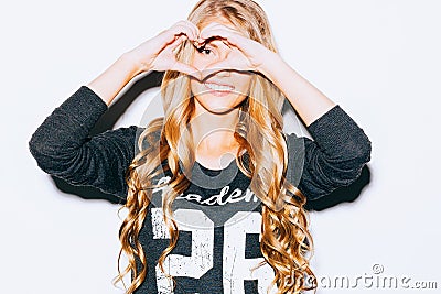 Love. Closeup portrait smiling happy young woman with long blon hair, making heart sign, symbol with hands white wall background. Stock Photo