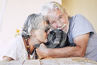 Love for dog and animals concept with couple of cheerful senior mature people and black funny pug in the middle - hug and Stock Photo