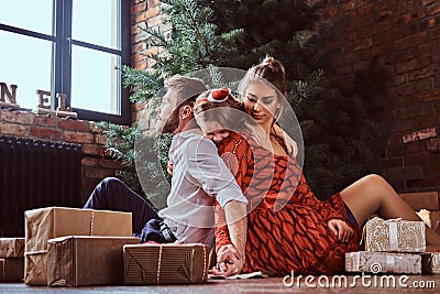 A happy little girl hugging her parents while they sit together on a floor surrounded by gifts next to the Christmas Stock Photo