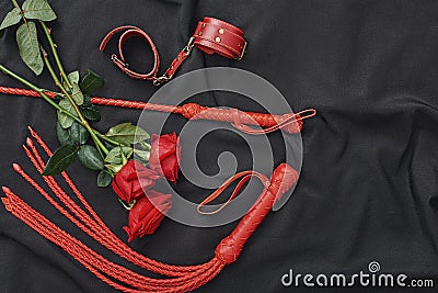 Love games. Top view of bdsm leather kit handcuffs, whip and beautiful red roses against of black silk fabric Stock Photo