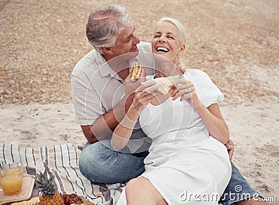 Love and healthy senior couple on picnic at a beach eating sandwich with funny conversation for wellness, healthcare or Stock Photo