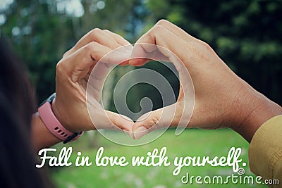 Love inspirational motivational quote - Fall in love with yourself. With hands making love sign against green nature park Stock Photo