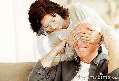 An elderly couple is in love as in their youth. A woman closes her eyes to her husband, wants to make a surprise. Stock Photo