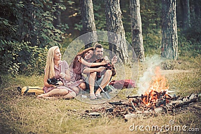 Love triangle and relations. Happy friends at campfire. Bearded man and women relax in forest. Hipster and girls in Stock Photo