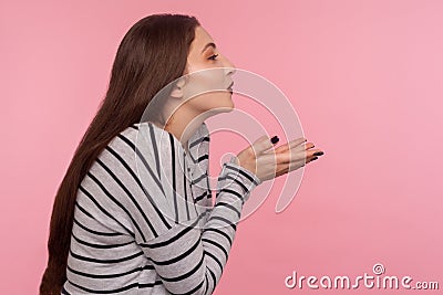 Love you! Side view of sensual attractive woman in striped sweatshirt sending air kiss over palms, expressing fondness Stock Photo