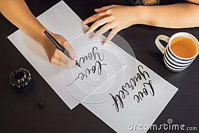 Love yourself. Calligrapher Young Woman writes phrase on white paper. Inscribing ornamental decorated letters Stock Photo