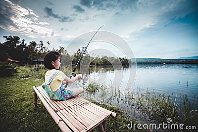 Happy girl pulling rod while fishing against landscape of lake. Stock Photo