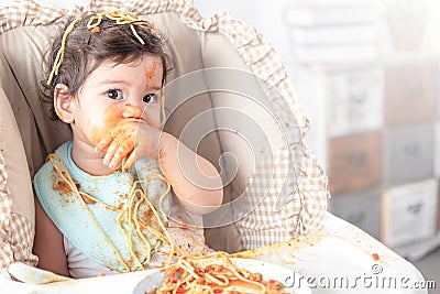 Lovely baby girl eating spaghetti and making a mess. Family leave baby alone, eating pasta herself Stock Photo