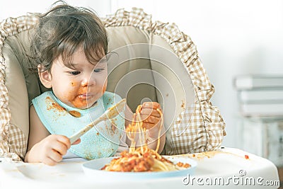 Lovely baby girl eating spaghetti and making a mess. Family leave baby alone, eating pasta herself Stock Photo