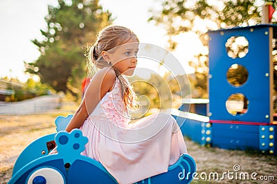 A lovely beautiful girl in a wonderful pink delicate dress sits on a small swing in a warm sunny summer park Stock Photo