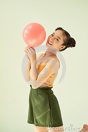 Lovely cheerful Asian teenager girl holding pink air balloon with two buns hairstyle over light background Stock Photo