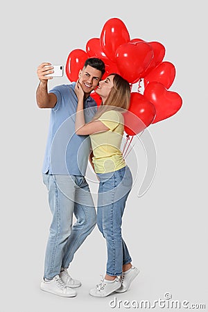 Lovely couple with heart shaped balloons taking selfie on light grey background. Valentine`s day celebration Stock Photo