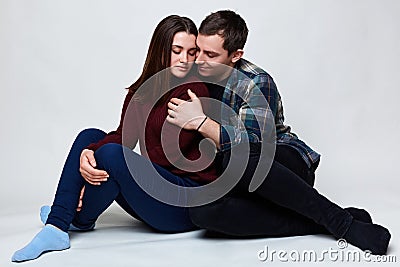 A lovely couple siting on the floor hugging each other with passion. A pretty woman closing her eyes from pleasure to be hugged by Stock Photo