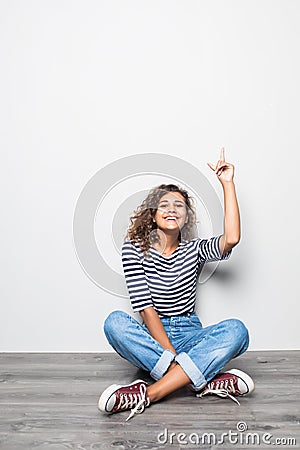 Lovely curly woman in casual clothes sitting in lotus pose on the floor being happy and candid over grey wall Stock Photo