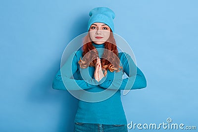 Lovely female makes request, keeps palms presses together, asks for something in close person, has calm expression, dressed Stock Photo