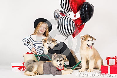 Lovely girl with blond hair wearing a hat with Malamute puppies with bright balloons hearts and gifts for Valentine`s Day Stock Photo